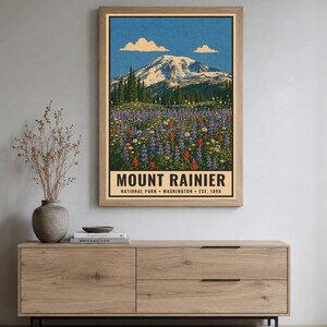 Op de afbeelding: Een verticale rechthoekige wandkunstprint met een landschapsillustratie van Mount Rainier met een besneeuwde top, groenblijvende bomen en een veld met paarse en rode wilde bloemen onder een blauwe lucht. De tekst luidt MOUNT RAINIER NATIONAL PARK WASHINGTON EST. 1899.