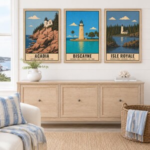 May include: Three framed vertical art prints featuring illustrations of lighthouses at Acadia, Biscayne, and Isle Royale National Parks. Each print includes the park name, location, and establishment year in black text at the bottom of the image.