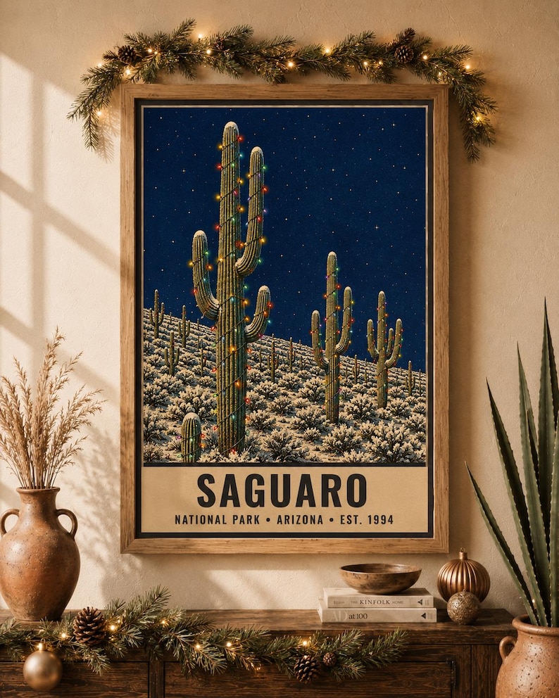 May include: A framed wall art print featuring a desert landscape at night with saguaro cacti wrapped in colorful string lights under a starry sky. The text at the bottom reads SAGUARO NATIONAL PARK ARIZONA EST. 1994 in a bold, dark font.