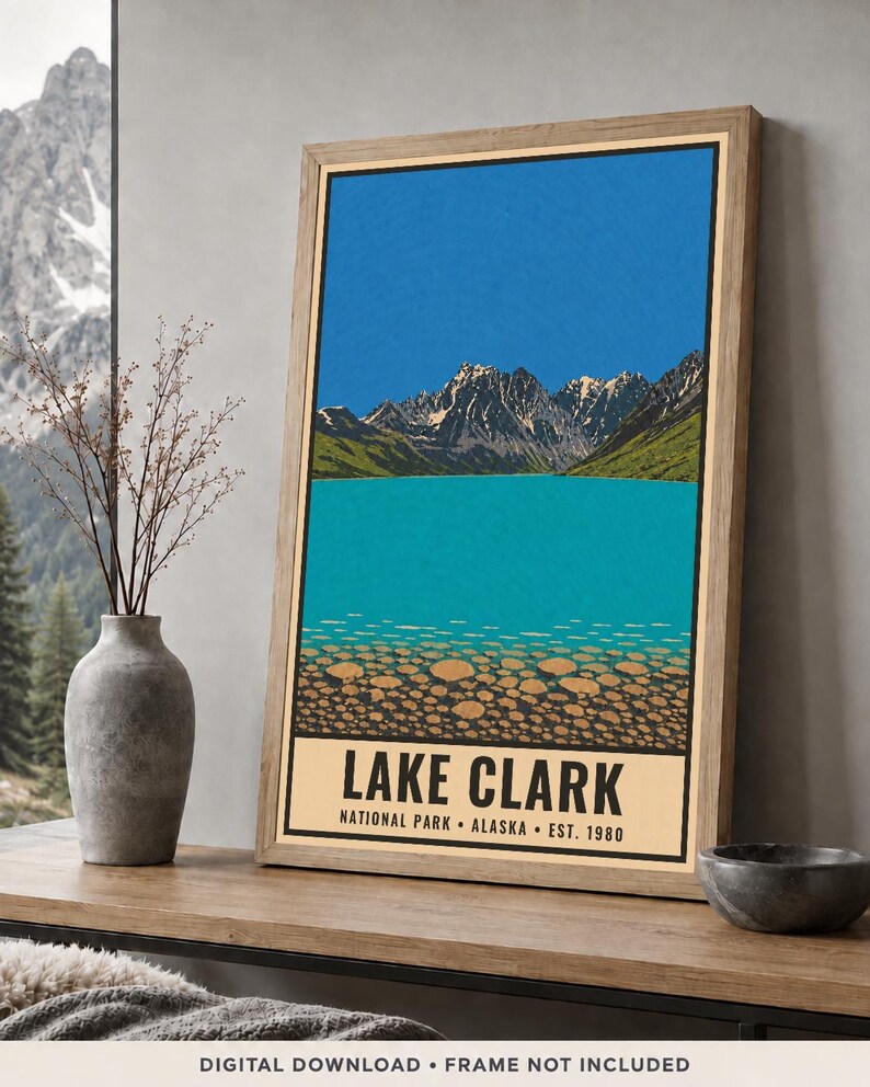 Pode incluir: Um cartaz vertical emoldurado com uma ilustra&ccedil;&atilde;o estilizada do Parque Nacional Lake Clark, no Alasca. A obra retrata um c&eacute;u azul brilhante, montanhas escarpadas com neve, um lago turquesa e um primeiro plano rochoso com o texto LAKE CLARK.