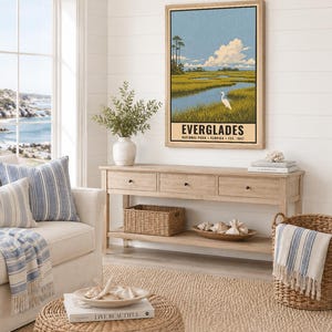 K&ouml;nnte beinhalten: Ein vertikaler Wandkunstdruck mit einer stilisierten Landschaft des Everglades-Nationalparks in Florida. Die Illustration zeigt ein sumpfiges Gew&auml;sser mit hohem Gras, einen wei&szlig;en Vogel und einen blauen Himmel mit Wolken. Der Text lautet EVERGLADES.