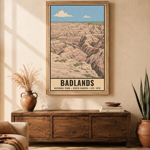 May include: A vertical wall art print featuring a landscape illustration of the Badlands National Park in South Dakota. The print displays layered rock formations under a blue sky with clouds and includes the text BADLANDS NATIONAL PARK SOUTH DAKOTA EST. 1978.