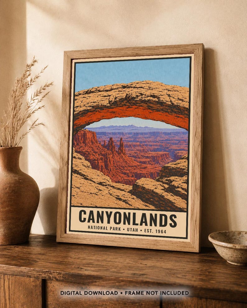 Może przedstawiać: Oprawiony plakat ze stylizowaną ilustracją łuku Mesa Arch w Parku Narodowym Canyonlands w stanie Utah. Grafika przedstawia czerwone formacje skalne pod niebieskim niebem, z napisem CANYONLANDS NATIONAL PARK UTAH EST. 1964 u dołu.