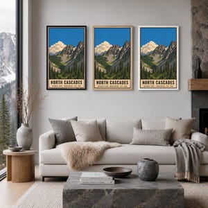 Op de afbeelding: Drie verticale wandkunstprints met een landschapsillustratie van North Cascades National Park, Washington, opgericht in 1968. Het kunstwerk toont grillige bergtoppen, groenblijvende bossen en een blauwe lucht met witte wolken.