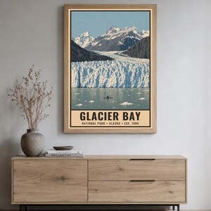 Pu&ograve; includere: Una stampa artistica da parete rettangolare con un paesaggio del Glacier Bay National Park in Alaska. L'immagine mostra montagne innevate, un grande ghiacciaio e un piccolo kayak sull'acqua. Il testo recita GLACIER BAY NATIONAL PARK ALASKA EST. 1980.