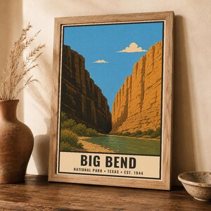 Op de afbeelding: Een ingelijste kunstdruk met een landschapsillustratie van Big Bend National Park in Texas. De afbeelding toont een rivier die stroomt tussen hoge, oranjebruine canyonwanden onder een helderblauwe lucht met twee kleine wolken en tekst onderaan.