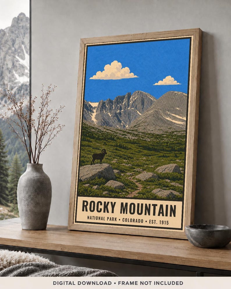 May include: A framed vertical poster featuring a landscape illustration of Rocky Mountain National Park, Colorado. The artwork depicts a bighorn sheep on a rock, green terrain, jagged mountains, and blue sky with clouds. Text reads: ROCKY MOUNTAIN NATIONAL PARK COLORADO EST. 1915.