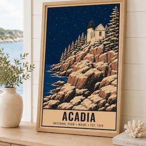 Puede incluir: Un p&oacute;ster enmarcado con una ilustraci&oacute;n nocturna de un faro en un acantilado rocoso en el Parque Nacional Acadia, Maine. La escena incluye rocas cubiertas de nieve, &aacute;rboles de hoja perenne con luces y un cielo estrellado. El texto dice ACADIA.