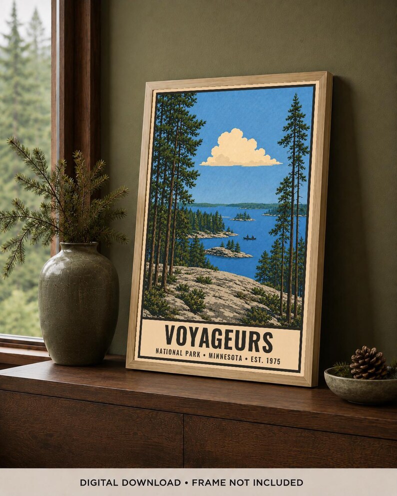 Op de afbeelding: Een ingelijste verticale kunstdruk met een landschapsillustratie van Voyageurs National Park in Minnesota. De afbeelding toont een rotsachtige kustlijn, hoge dennenbomen, een blauw meer met kleine eilanden en een wolk. De tekst luidt VOYAGEURS NATIONAL PARK MINNESOTA EST. 1975.