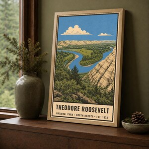 May include: A framed vertical art print depicting a landscape of Theodore Roosevelt National Park in North Dakota. The illustration features a winding blue river through green terrain and tan cliffs under a blue sky with white clouds. Text reads: THEODORE ROOSEVELT NATIONAL PARK &bull; NORTH DAKOTA &bull; EST. 1978.