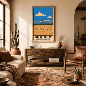 Op de afbeelding: Een rechthoekige wandkunstprint met een landschapsillustratie van Kobuk Valley National Park, Alaska. Het ontwerp toont een helderblauwe lucht met wolken, besneeuwde bergen, een donkere bosrand en een beige woestijn met silhouetten van kariboes.