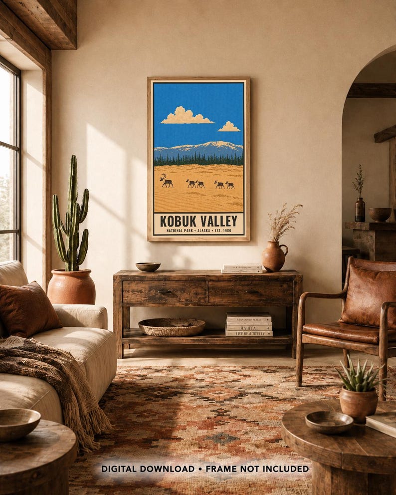Op de afbeelding: Een rechthoekige wandkunstprint met een landschapsillustratie van Kobuk Valley National Park, Alaska. Het ontwerp toont een helderblauwe lucht met wolken, besneeuwde bergen, een donkere bosrand en een beige woestijn met silhouetten van kariboes.