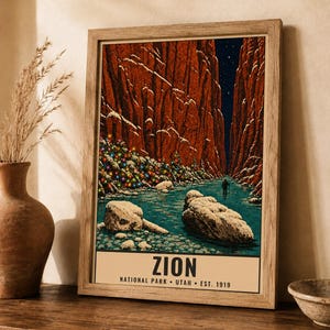 May include: A framed art print featuring a snowy Zion National Park canyon scene with a river, red rock cliffs, a starry night sky, and a decorated Christmas tree. The text at the bottom reads ZION NATIONAL PARK &bull; UTAH &bull; EST. 1919.