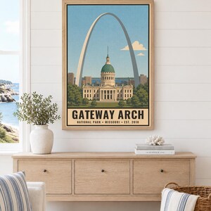 Op de afbeelding: Een ingelijste wandkunstprint met een gestileerde illustratie van de Gateway Arch en het Old Courthouse in St. Louis, Missouri. De tekst luidt GATEWAY ARCH NATIONAL PARK MISSOURI EST. 2018. De print heeft een lichtblauwe lucht.