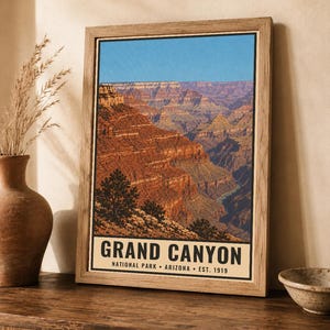 K&ouml;nnte beinhalten: Ein gerahmtes vertikales Poster mit einer Landschaftsansicht des Grand Canyon mit geschichteten roten Felsformationen unter einem klaren blauen Himmel. Der Text unten lautet GRAND CANYON NATIONAL PARK ARIZONA EST. 1919 in fetten schwarzen Gro&szlig;buchstaben.