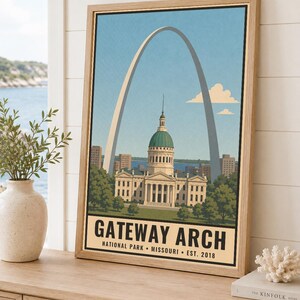 May include: A framed vertical art print featuring a stylized illustration of the Gateway Arch and the Old Courthouse in St. Louis, Missouri. The text at the bottom reads GATEWAY ARCH NATIONAL PARK MISSOURI EST. 2018 in bold black lettering.