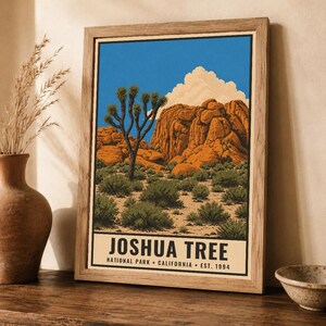 May include: A framed art print featuring a desert landscape with a Joshua tree, large orange rock formations, and a bright blue sky with white clouds. The text at the bottom reads JOSHUA TREE NATIONAL PARK CALIFORNIA EST. 1994 in black font.