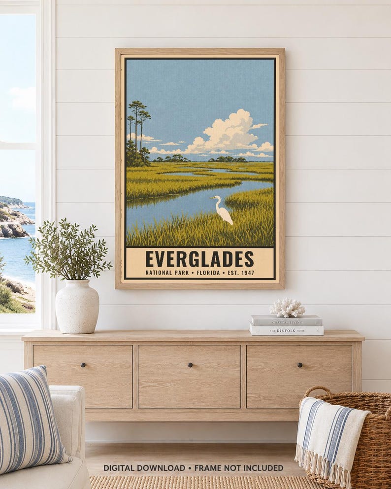 K&ouml;nnte beinhalten: Ein gerahmtes vertikales Poster, das den Everglades Nationalpark in Florida darstellt. Die Illustration zeigt einen wei&szlig;en Reiher in einem grasbewachsenen Sumpfgebiet unter einem blauen, bew&ouml;lkten Himmel. Der Text lautet EVERGLADES NATIONAL PARK FLORIDA EST. 1947.