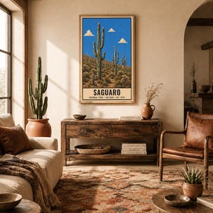Op de afbeelding: Een verticale wandkunstprint met een woestijnlandschap met hoge groene saguaro-cactussen onder een helderblauwe lucht met kleine wolken. Het onderste gedeelte heeft een cr&egrave;mekleurige rand met de tekst SAGUARO NATIONAL PARK ARIZONA EST. 1994.