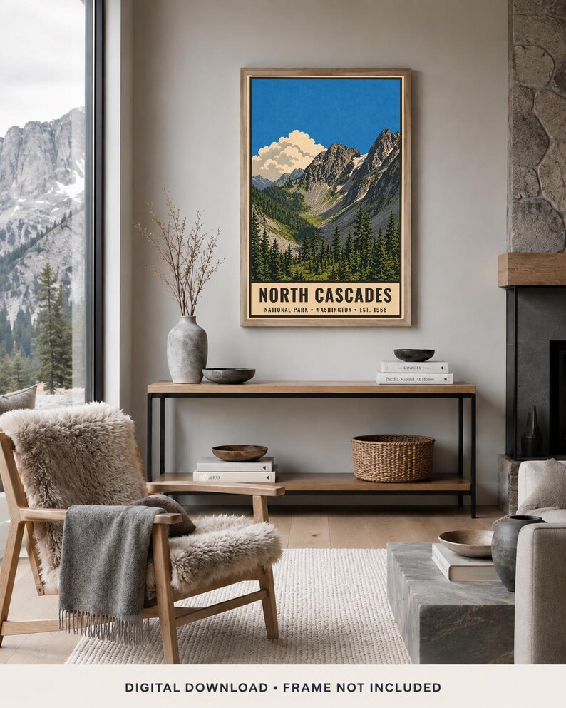 Op de afbeelding: Een ingelijste verticale wandkunstprint van het North Cascades National Park in Washington, opgericht in 1968. De illustratie toont grillige bergtoppen, een helderblauwe lucht met witte wolken en een dicht bos met groene dennenbomen.