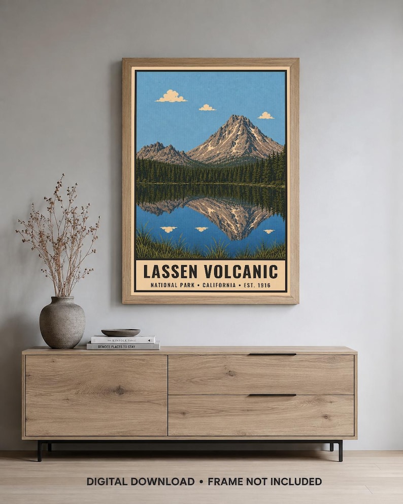 K&ouml;nnte beinhalten: Ein gerahmter Wandkunstdruck mit einer Landschaftsillustration des Lassen Volcanic Nationalparks in Kalifornien. Das Bild zeigt einen Berggipfel, der sich in einem See spiegelt, mit blauem Himmel, Wolken und dem Text LASSEN VOLCANIC NATIONAL PARK.