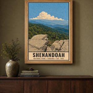 Op de afbeelding: Een ingelijste poster met een landschapsillustratie van Shenandoah National Park in Virginia. Het kunstwerk toont rotsachtige kliffen, een hert, groene bossen en blauwe bergen onder een bewolkte lucht. De tekst luidt SHENANDOAH NATIONAL PARK VIRGINIA EST. 1935.