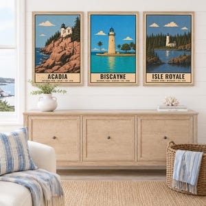 Może przedstawiać: Trzy oprawione pionowe wydruki artystyczne z ilustracjami latarni morskich w parkach narodowych Acadia, Biscayne i Isle Royale. Każdy wydruk zawiera nazwę parku, lokalizację i rok założenia czarnym tekstem u dołu obrazu.