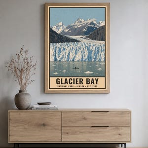 Może przedstawiać: Prostokątny wydruk ścienny przedstawiający krajobraz Parku Narodowego Glacier Bay na Alasce. Obraz ukazuje ośnieżone g&oacute;ry, wielki lodowiec oraz mały kajak na wodzie. Tekst głosi GLACIER BAY NATIONAL PARK ALASKA EST. 1980.