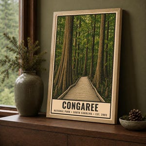 May include: A framed vertical poster featuring a detailed illustration of a wooden boardwalk winding through a dense forest of tall trees. The text at the bottom reads CONGAREE NATIONAL PARK SOUTH CAROLINA EST. 2003 in bold black capital letters.