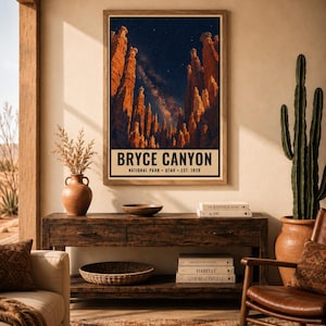 May include: A vertical wall art print featuring a night sky over Bryce Canyon, Utah, with orange rock formations and a starry Milky Way. The text reads BRYCE CANYON NATIONAL PARK UTAH EST. 1928. The print is displayed in a wooden frame on a wall.
