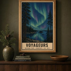 Może przedstawiać: Oprawiony pionowy plakat przedstawiający nocną scenerię Parku Narodowego Voyageurs w Minnesocie, założonego w 1975 roku. Grafika ukazuje ciemnoniebieskie jezioro odbijające żywe zielone i fioletowe zorze polarne nad lasem sosnowym.