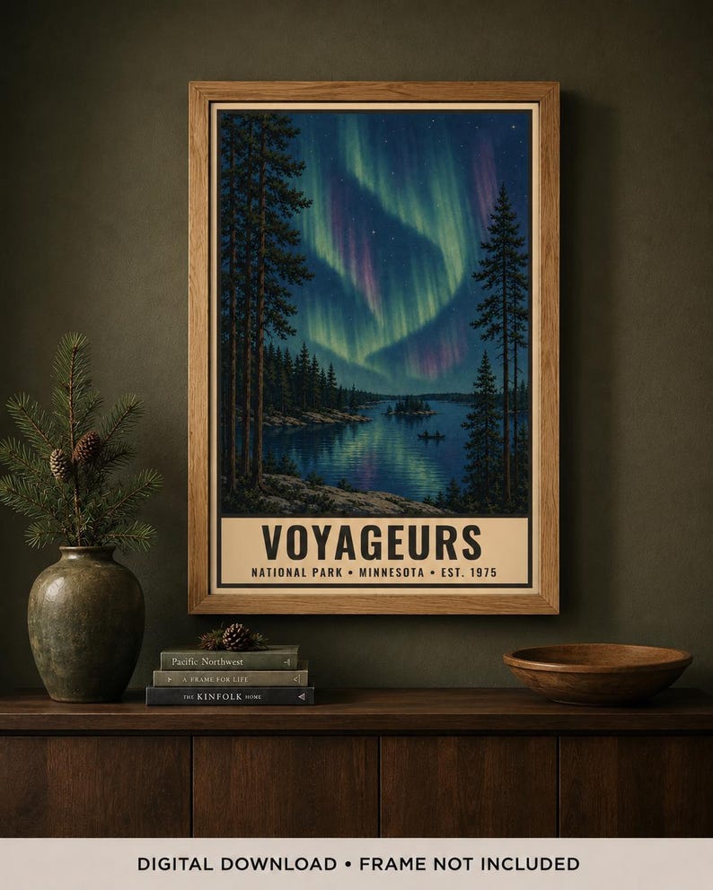 Może przedstawiać: Oprawiony pionowy plakat przedstawiający nocną scenerię Parku Narodowego Voyageurs w Minnesocie, założonego w 1975 roku. Grafika ukazuje ciemnoniebieskie jezioro odbijające żywe zielone i fioletowe zorze polarne nad lasem sosnowym.