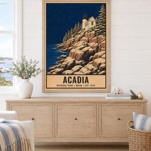 Puede incluir: Una l&aacute;mina de arte mural enmarcada que muestra un paisaje nocturno del Parque Nacional Acadia en Maine. La ilustraci&oacute;n representa un faro en un acantilado rocoso con &aacute;rboles de hoja perenne bajo un cielo estrellado. El texto dice ACADIA NATIONAL PARK MAINE EST. 1919.