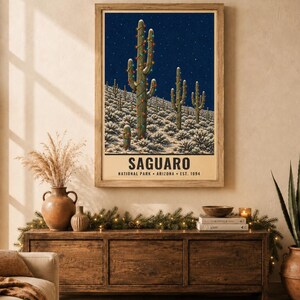 May include: A rectangular wall art print featuring a dark blue night sky over a desert landscape with snow-covered ground and saguaro cacti decorated with colorful string lights. The text reads SAGUARO NATIONAL PARK ARIZONA EST. 1994.