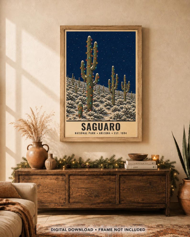 May include: A rectangular wall art print featuring a dark blue night sky over a desert landscape with snow-covered ground and saguaro cacti decorated with colorful string lights. The text reads SAGUARO NATIONAL PARK ARIZONA EST. 1994.