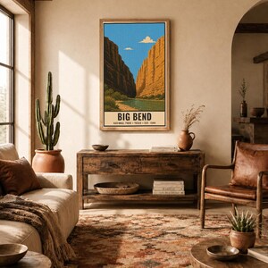 Op de afbeelding: Een verticale rechthoekige wandkunstprint met een gestileerde illustratie van Big Bend National Park. Het kunstwerk toont een rivier die tussen hoge canyonwanden stroomt onder een blauwe lucht met wolken. De tekst luidt BIG BEND NATIONAL PARK TEXAS EST. 1944.