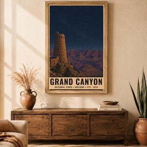 May include: A rectangular wall art print featuring a night scene of the Grand Canyon with a stone watchtower under a starry sky. The text reads GRAND CANYON NATIONAL PARK ARIZONA EST. 1919. The print is displayed in a light wood frame.