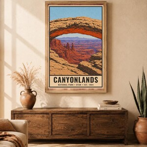 Op de afbeelding: Een verticale wandkunstprint met een gestileerde illustratie van Mesa Arch in Canyonlands National Park, Utah. De tekst luidt CANYONLANDS NATIONAL PARK UTAH EST. 1964. De afbeelding toont een natuurlijke rotsboog die een woestijnkloof omlijst.