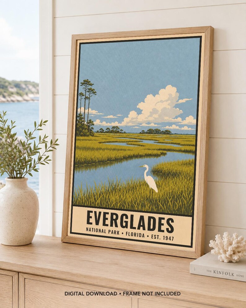 K&ouml;nnte beinhalten: Ein gerahmtes vertikales Poster mit einer Landschaftsillustration des Everglades-Nationalparks in Florida. Das Kunstwerk zeigt einen wei&szlig;en Reiher in einem grasbewachsenen Sumpfgebiet mit einem gewundenen blauen Wasserlauf, hohen B&auml;umen und Wolken.