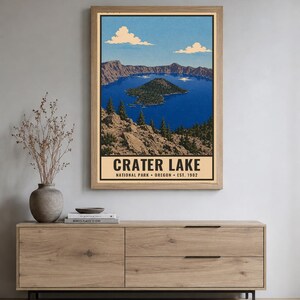 Op de afbeelding: Een verticale wandkunstprint met een gestileerde illustratie van Crater Lake National Park in Oregon. De afbeelding toont een diepblauw meer met Wizard Island, omringd door rotsachtige kliffen en dennenbomen onder een blauwe lucht met witte wolken.