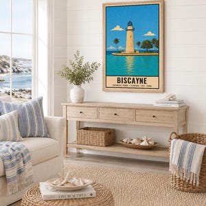 May include: A framed vertical wall art print featuring a stylized illustration of a lighthouse on a small island surrounded by turquoise water under a bright blue sky, with the text BISCAYNE NATIONAL PARK FLORIDA EST. 1980 printed at the bottom.
