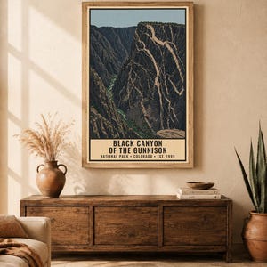 Op de afbeelding: Een verticale wandkunstprint met een gestileerde illustratie van het Black Canyon of the Gunnison National Park in Colorado, met donkere rotsachtige kliffen, een rivier en de tekst Black Canyon of the Gunnison National Park Colorado Est. 1999.