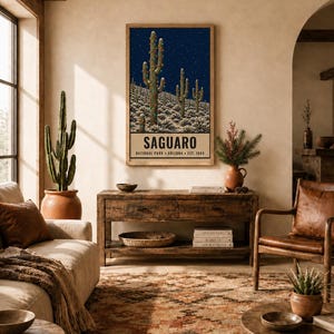 May include: A rectangular wall art print featuring a dark blue night sky with stars over a desert landscape of saguaro cacti. The bottom section contains the text SAGUARO NATIONAL PARK ARIZONA EST. 1994 in black capital letters on a cream background.