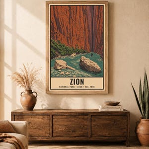 Op de afbeelding: Een verticale wandkunstprint met een gestileerde illustratie van Zion National Park met torenhoge rode canyonwanden, een turquoise rivier en grote rotsblokken. De tekst luidt ZION NATIONAL PARK UTAH EST. 1919. Ingelijst in een houten lijst.