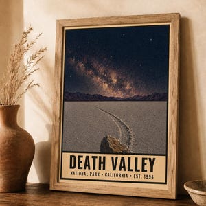 May include: A framed vertical poster featuring a night sky with a visible Milky Way galaxy over the Death Valley desert landscape, including a rock with a trail on the cracked ground. The text reads DEATH VALLEY NATIONAL PARK CALIFORNIA EST. 1994.