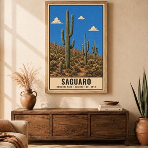 Op de afbeelding: Een verticale wandkunstprint met een woestijnlandschap met hoge groene saguaro-cactussen onder een helderblauwe lucht met witte wolken. Het onderste gedeelte bevat de tekst SAGUARO NATIONAL PARK ARIZONA EST. 1994 in een vetgedrukt zwart lettertype.