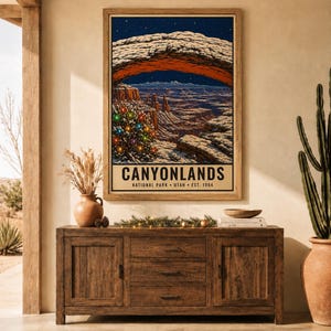 May include: A framed vertical poster print featuring a night landscape of Canyonlands National Park in Utah. The artwork displays a natural stone arch, a starry sky, and a decorated Christmas tree with colorful lights. Text reads CANYONLANDS.