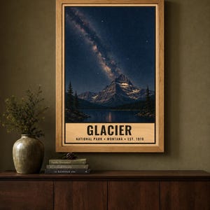 May include: A framed vertical poster featuring a night landscape of Glacier National Park in Montana. The image displays a mountain peak under a starry sky with the Milky Way, a lake, and pine trees. Text reads: GLACIER NATIONAL PARK MONTANA EST. 1910.