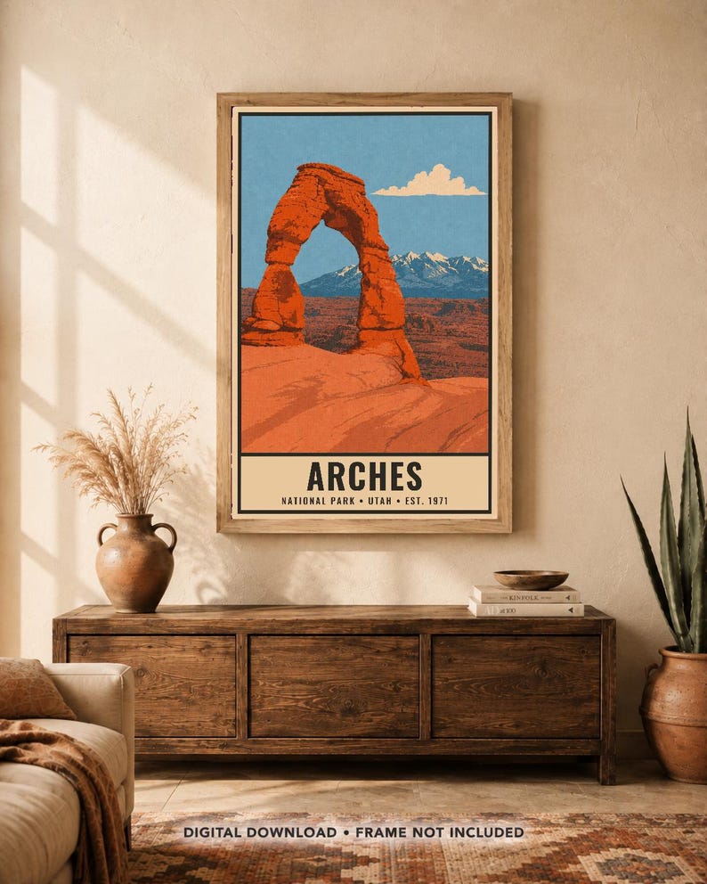 Op de afbeelding: Een verticale wandkunstprint met een gestileerde illustratie van de rode rotsboog Delicate Arch in Arches National Park, Utah. De tekst onderaan luidt ARCHES NATIONAL PARK UTAH EST. 1971. De print toont een blauwe lucht en bergen.