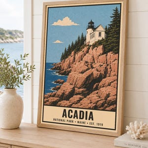 May include: A framed travel poster print featuring a lighthouse perched on rocky cliffs above a blue ocean, with evergreen trees and a light blue sky. The text at the bottom reads ACADIA NATIONAL PARK MAINE EST. 1919 in bold black lettering.